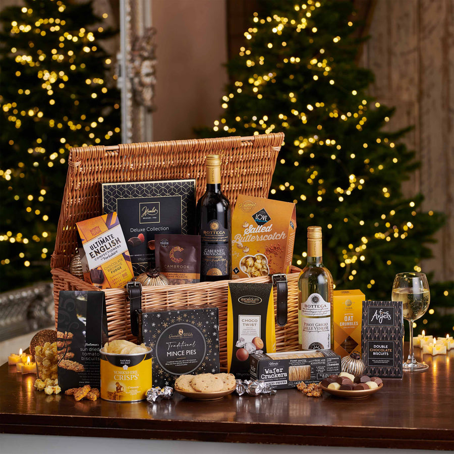 The Fireside Feast Hamper with wine, chocolate and mince pies opened on a table top in front of a Christmas tree.